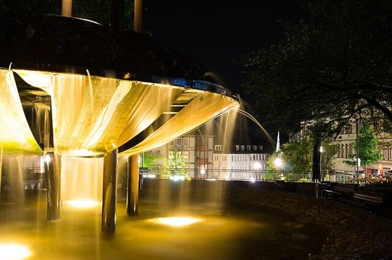 Beleuchteter Brunnen mit herabfließendem Wasser bei Nacht in der Innenstadt von Siegen.
