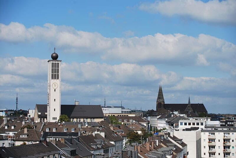 Stadtansicht von Solingen mit markantem Uhrenturm und dicht bebauten Wohnhäusern unter Wolkenhimmel.