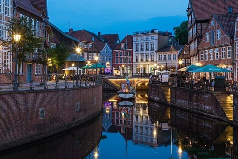 Spiegelnder Kanal zwischen historischen Gebäuden und Brücken in der Altstadt von Stade bei Dämmerung.
