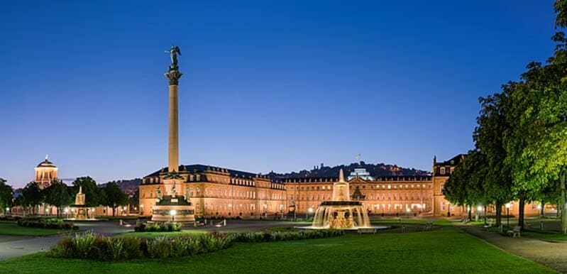 Coreflow-Stuttgart-Hero Weitläufiger Schlossplatz in Stuttgart mit Grünflächen, Brunnen und hell erstrahlender Fassade zur Blauen Stunde.