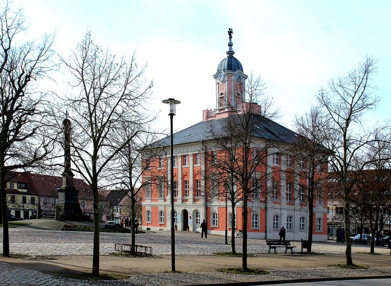 Coreflow-Templin-Hero Historisches Rathaus in Templin mit rosa Fassade, Turmaufsatz und kahlen Bäumen auf dem Marktplatz.