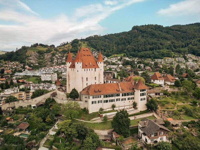 Schloss Thun mit markanten Türmen auf Anhöhe, umgeben von Stadt und grüner Hügellandschaft.