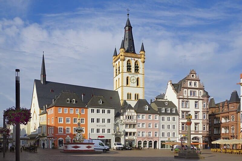 Marktplatz mit farbigen historischen Häusern, Kirchturm und geöffneten Sonnenschirmen bei Tageslicht in Trier.