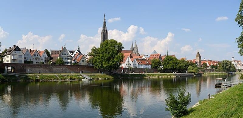 Coreflow-Ulm-Hero Blick auf Ulms Altstadt mit Münsterturm und Uferbereich, der sich im ruhigen Wasser spiegelt.