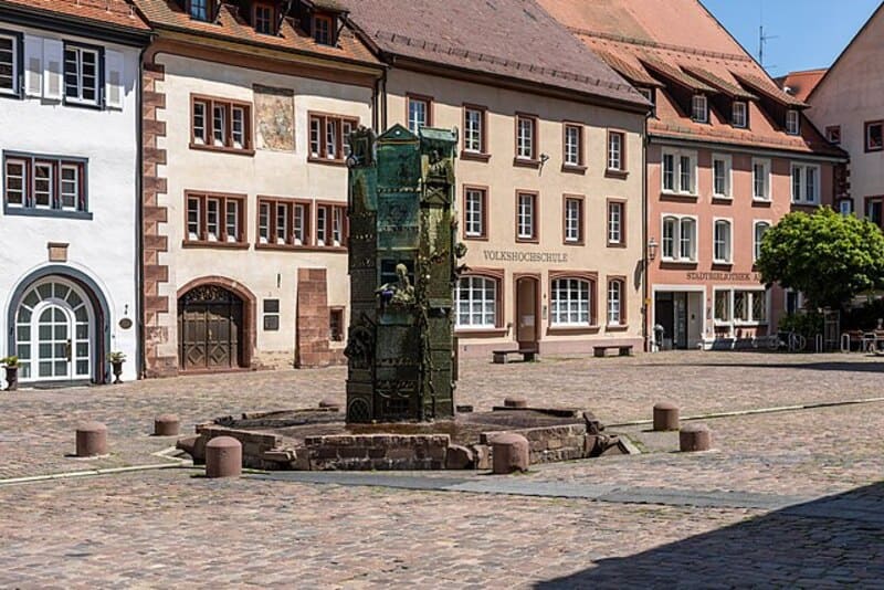 Platz in Villingen-Schwenningen mit historischem Brunnen und umliegenden Gebäuden unter klarem Himmel.