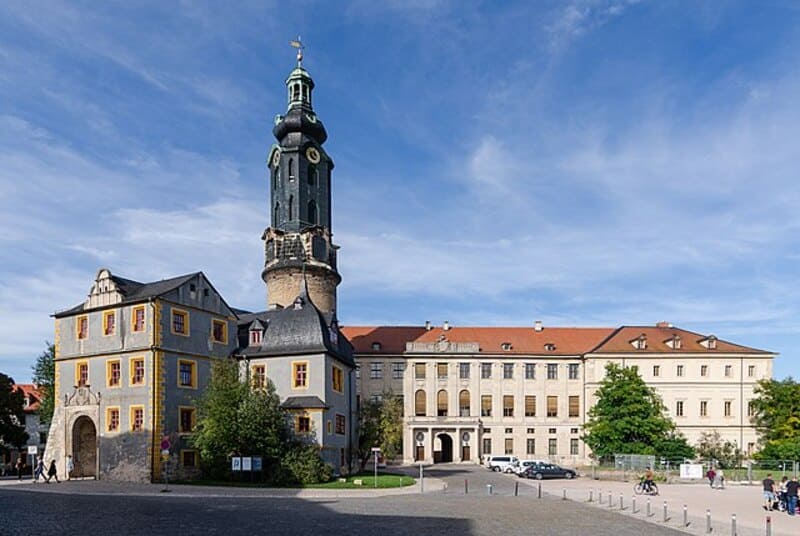 Blick auf das Stadtschloss Weimar mit markantem Turm und hellem Hauptgebäude unter blauem Himmel.