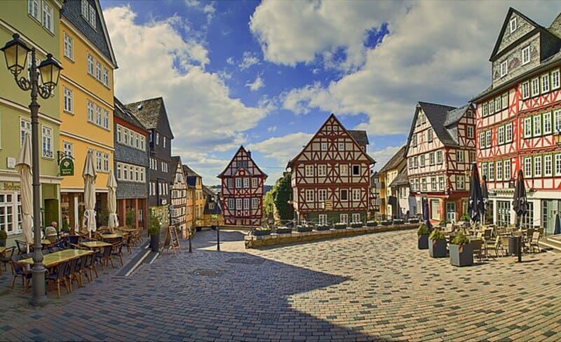 Historischer Marktplatz in Wetzlar mit farbigen Fachwerkhäusern und Außengastronomie unter blauem Himmel.