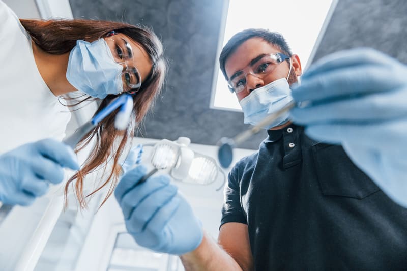 Coreflow-Zahnarzt-Hero Medizinisches Personal mit Schutzkleidung hält Instrumente und schaut von oben in Behandlungsraum.