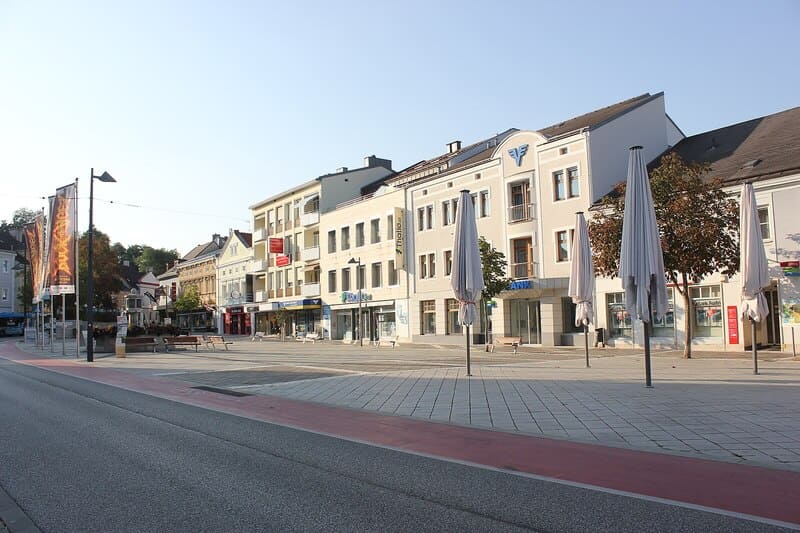 Coreflow_Amstetten_SEO_Hero Stadtzentrum von Amstetten mit breitem Platz, Straßenrand, Caféschirmständern und mehrgeschossigen Häusern.