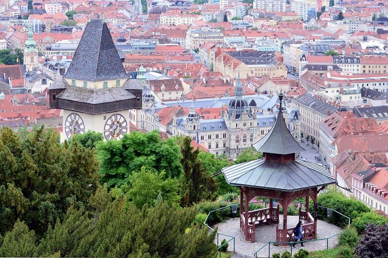 Blick über Graz mit Uhrturm am Schlossberg, Pavillon im Vordergrund und dichter Altstadtbebauung.