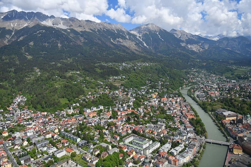 Luftaufnahme von Innsbruck mit dicht bebauter Stadt, Inn-Fluss und Alpen im Hintergrund.