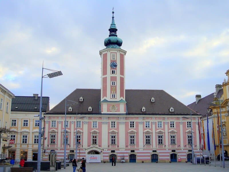 Rathaus St. Pölten mit rosafarbener Fassade, Uhrturm und offenem Hauptplatz im Vordergrund.